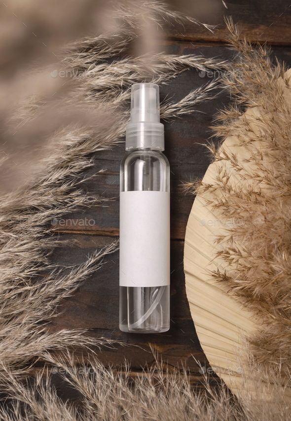 Cosmetic spray bottle on wood near palm leaf and pampas grass top view. Label Mockup