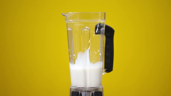 Closeup Blender with Milk at Yellow Background and Red Strawberries Falling in Slow Motion in Liquid alt