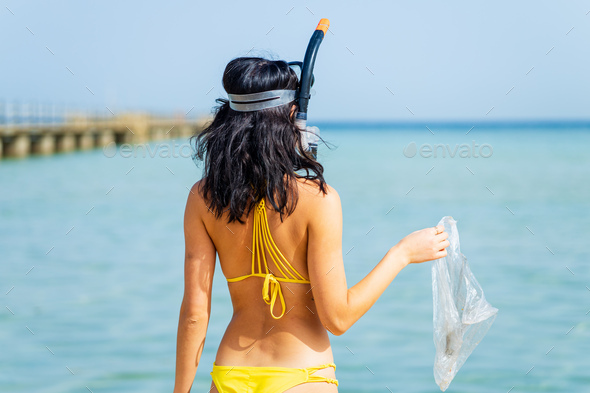 woman in yellow bikini and scuba picking up a plastic trash from sea