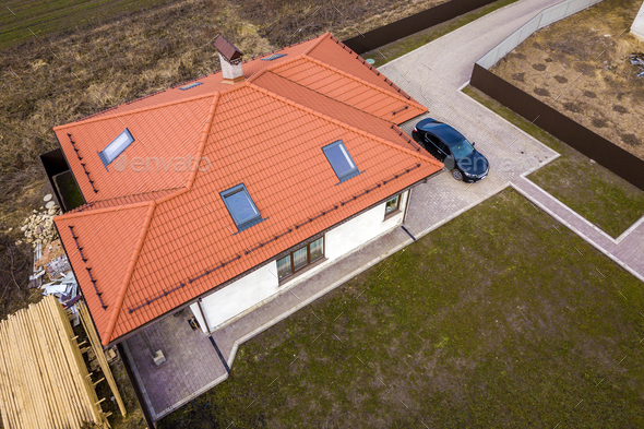Aerial top view of house metal shingle roof with attic windows and black car on paved yard.