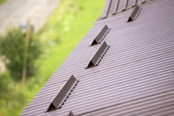 Metal brown shingle tiling house roof surface, rain gutter pipe and snow guards protective fence.