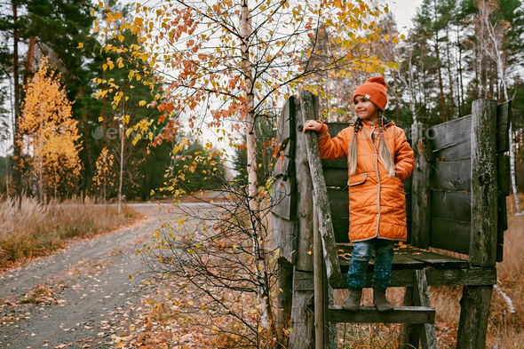 Happy girl in orange coat walks and plays in handmade wooden house in autumn park. Active weekend