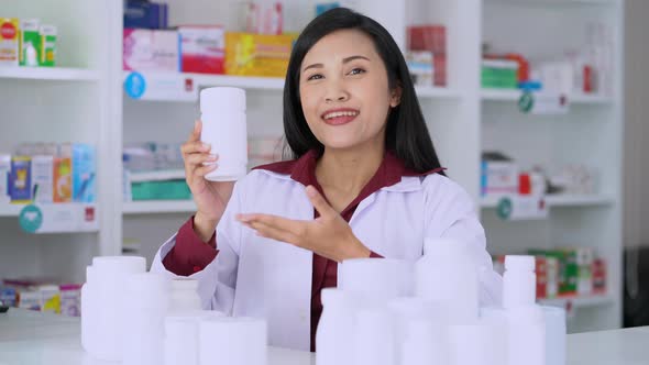 A woman pharmacist look a camera explaining each bottle of medicine in pharmacy center	