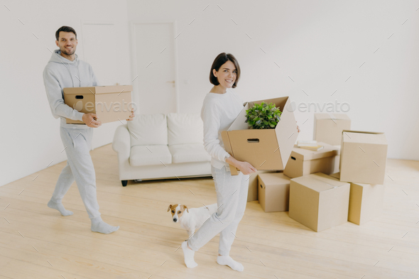 smiling brunette woman and her husband carry cardboard boxes with personal belongings