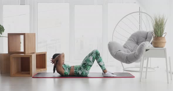 Sporty black woman is doing abs exercises on floor at home.