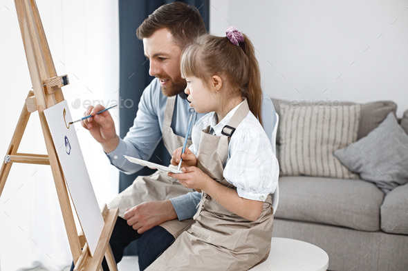 Girl with Down syndrome and her father painting on an easel with brushes