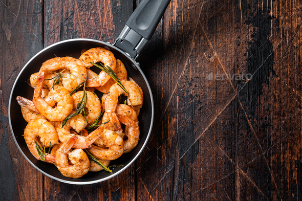 Fried with butter and garlic prawns shrimps in a skillet. Wooden background. Top view. Copy space