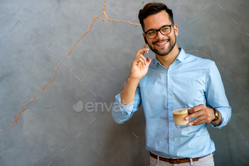 Portrait of a smiling young business man using smartphone and holding cup of coffee