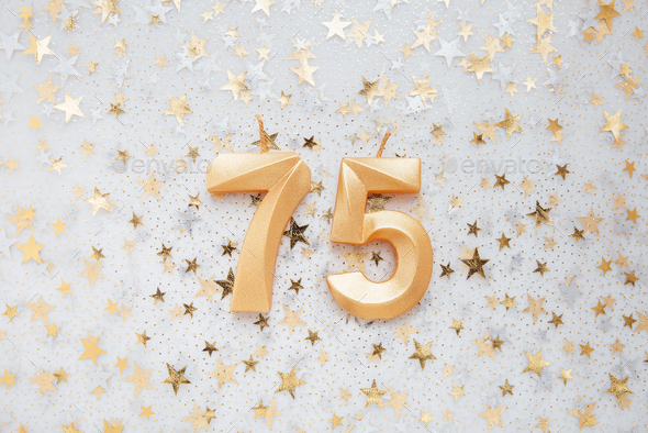 Number 75 seventy five golden celebration birthday candle on Festive Background.
