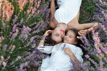 Mom and daughter in white dresses are lying in a lavender field. Provence.