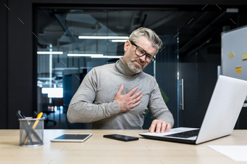 businessman heart attack at workplace, mature gray haired man working on laptop has severe chest