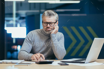Upset and disappointed senior and mature financier, man working inside office building, calculating