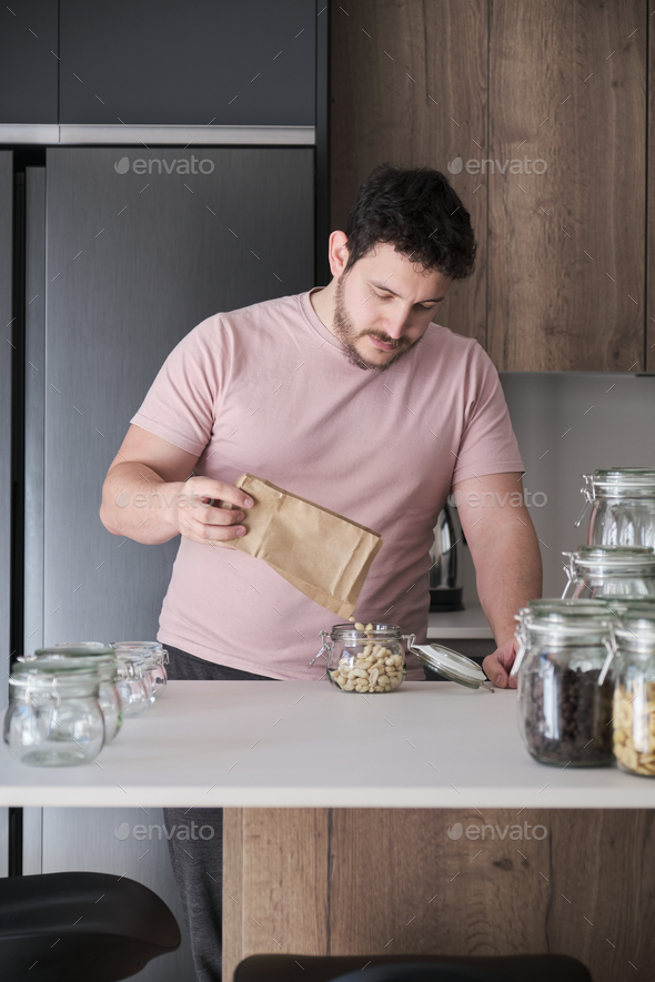 Young latin man filling up a jar with peeled peanuts from a paper bag.