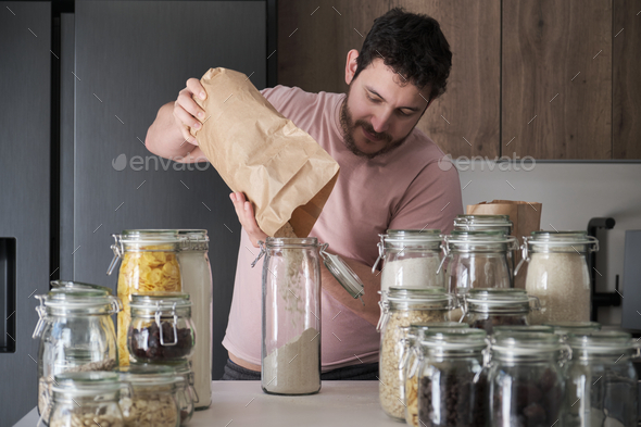 Young latin man filling up a jar with whole wheat flour from a paper bag.