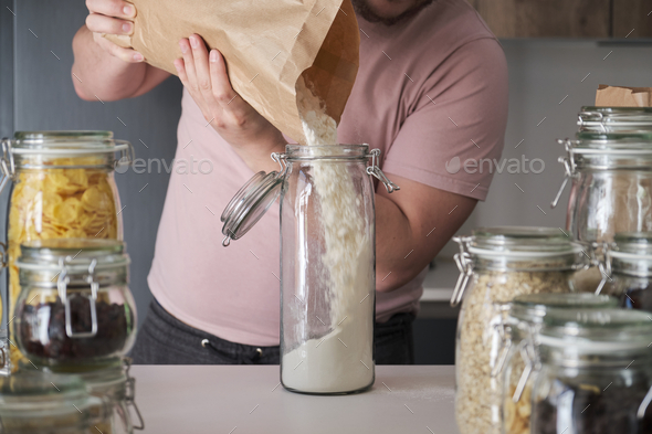 Unrecognizable latin man filling up a jar with wheat flour from a paper bag.