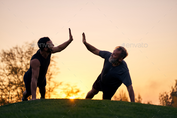 The two sportsmen push up together on the sunset background.