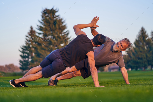 The young and old sportsmen push up together on the grass.
