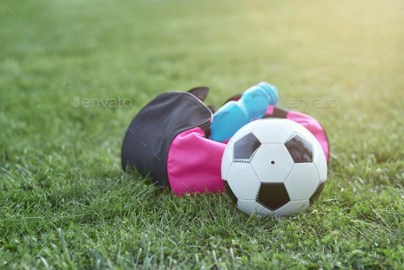 Soccer ball, bottle of water and sports bag on green grass