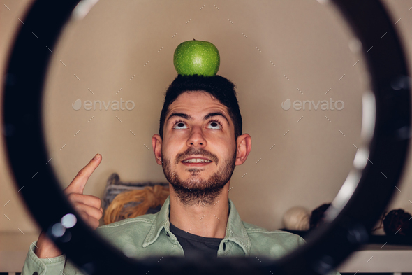 Male nutritionist with a green apple on his head in a funny way while recording a video in his home