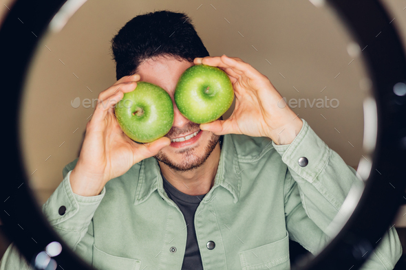 Funny face of a nutritionist man with two green apples in his eyes while recording a video