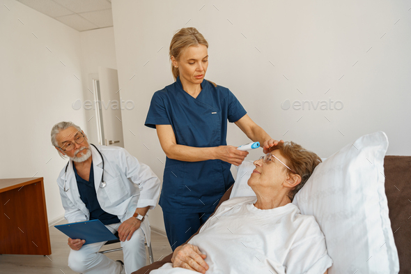 Doctor measures patient\'s temperature with non-contact thermometer in hospital ward