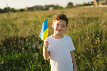 Ukrainian child boy in white t shirt with yellow and blue flag of Ukraine in field.