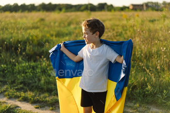Ukrainian child boy in white t shirt with yellow and blue flag of Ukraine in field.