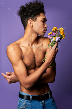 Sensual latino male with bouquet portrait. Athletic transgender male model on purple background