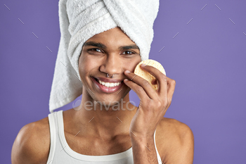 Portrait of handsome man cleaning face and looking camera with cosmetic pads on purple background