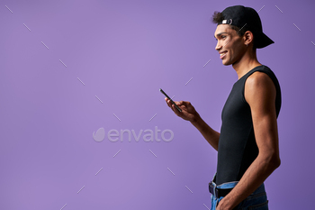 Transgender smiling male with mobile in hand side view on purple background portrait