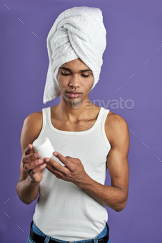 Transgender young man with face cream in hand and towel on head portrait