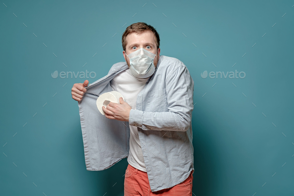 Man in medical mask in panic hides toilet paper under shirt, fears quarantine during virus outbreak