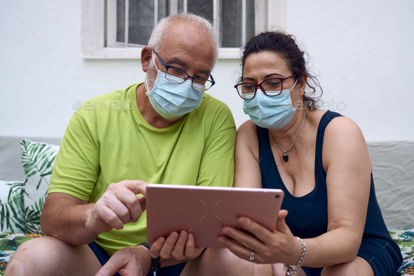 Older couple wearing a surgical masks making a video call with a tablet