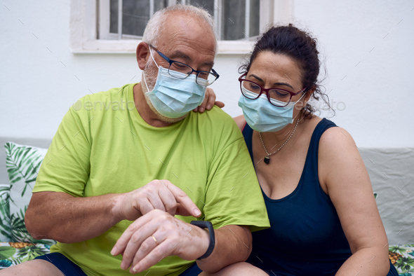 Older couple wearing a surgical masks using a smart watch