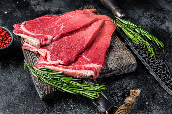 Raw fresh beef meat round steak with herbs and spices. Black background. Top view