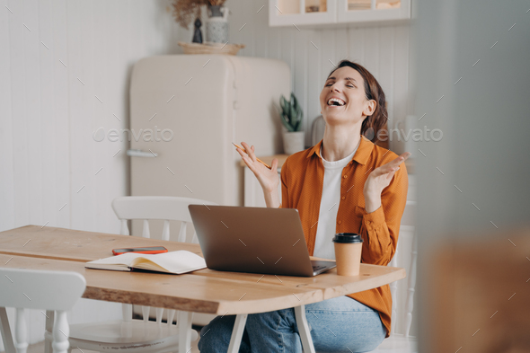 Girl received good news, promotion at work, rejoices achievement of goal, sitting at laptop at home
