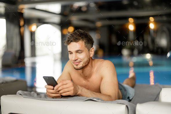 Man rests with phone by the swimming pool indoors at spa resort Stock ...