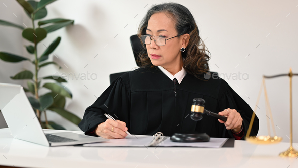 Focused senior female lawyer in robe gown uniform sitting front of ...