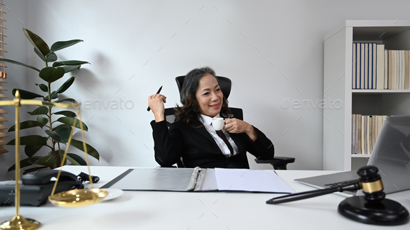 Experienced mature female lawyer sitting in her personal office and watching online on laptop
