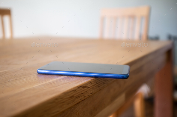 Smartphone is carelessly left on the edge of a wooden table and can fall