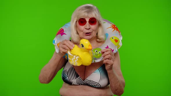 Senior Woman Tourist in Sunglasses Dancing Playing with Inflatable Duck Toy Rubber Swimming Ring alt