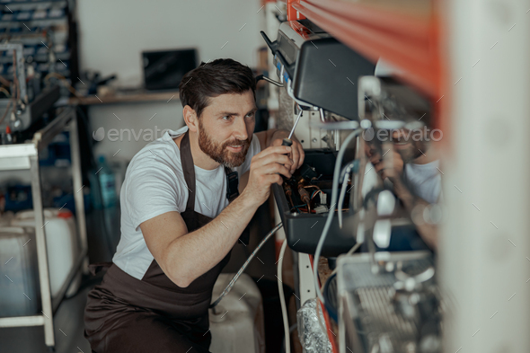 Smiling young man repairing coffee machine using screwdriver in a workshop