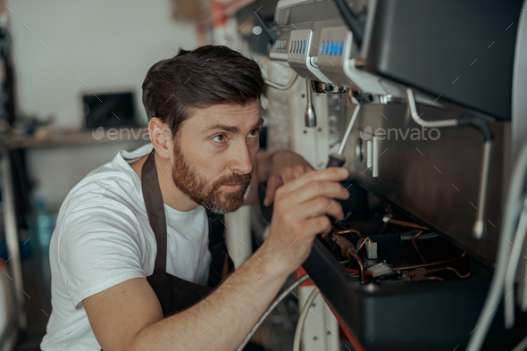 Close up of young man repairing coffee machine using screwdriver in a workshop