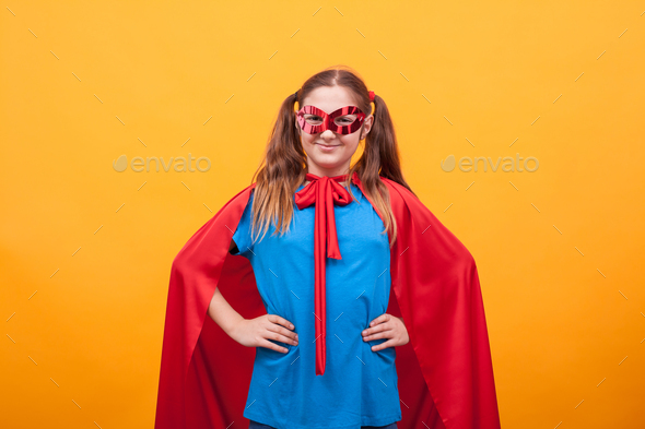 Little girl in super hero costume ready to save the world from bad guys over yellow background