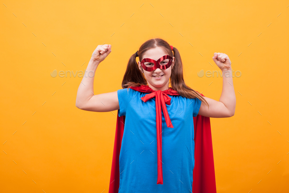 Little in superman costume showing her muscles over yellow background
