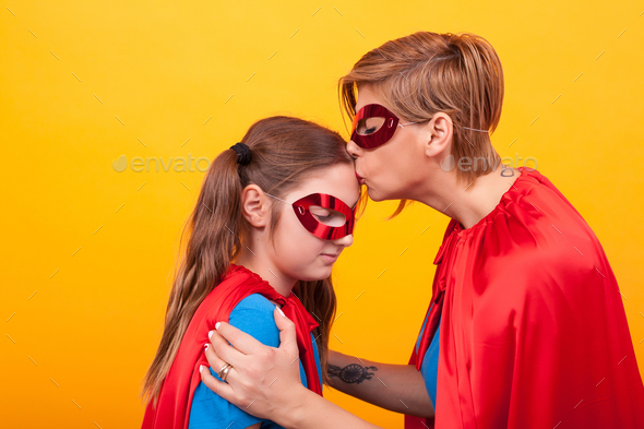 Mother in superman costume kissing hes little girl forehead over yellow background