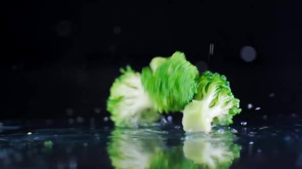 Broccoli falling on wet surface splashing drops in slow motion 