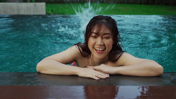 woman hold on to the edge of the swimming pool and splashing water with her feet