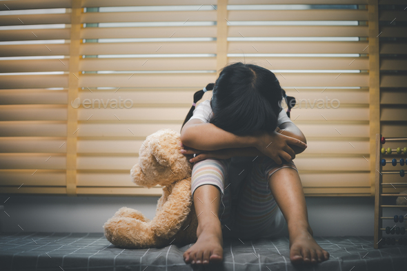 Close up lonely little girl hugging toy, sitting at home alone, upset unhappy child
