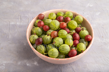 Fresh red and green gooseberry in ceramic bowl on gray concrete, side view.